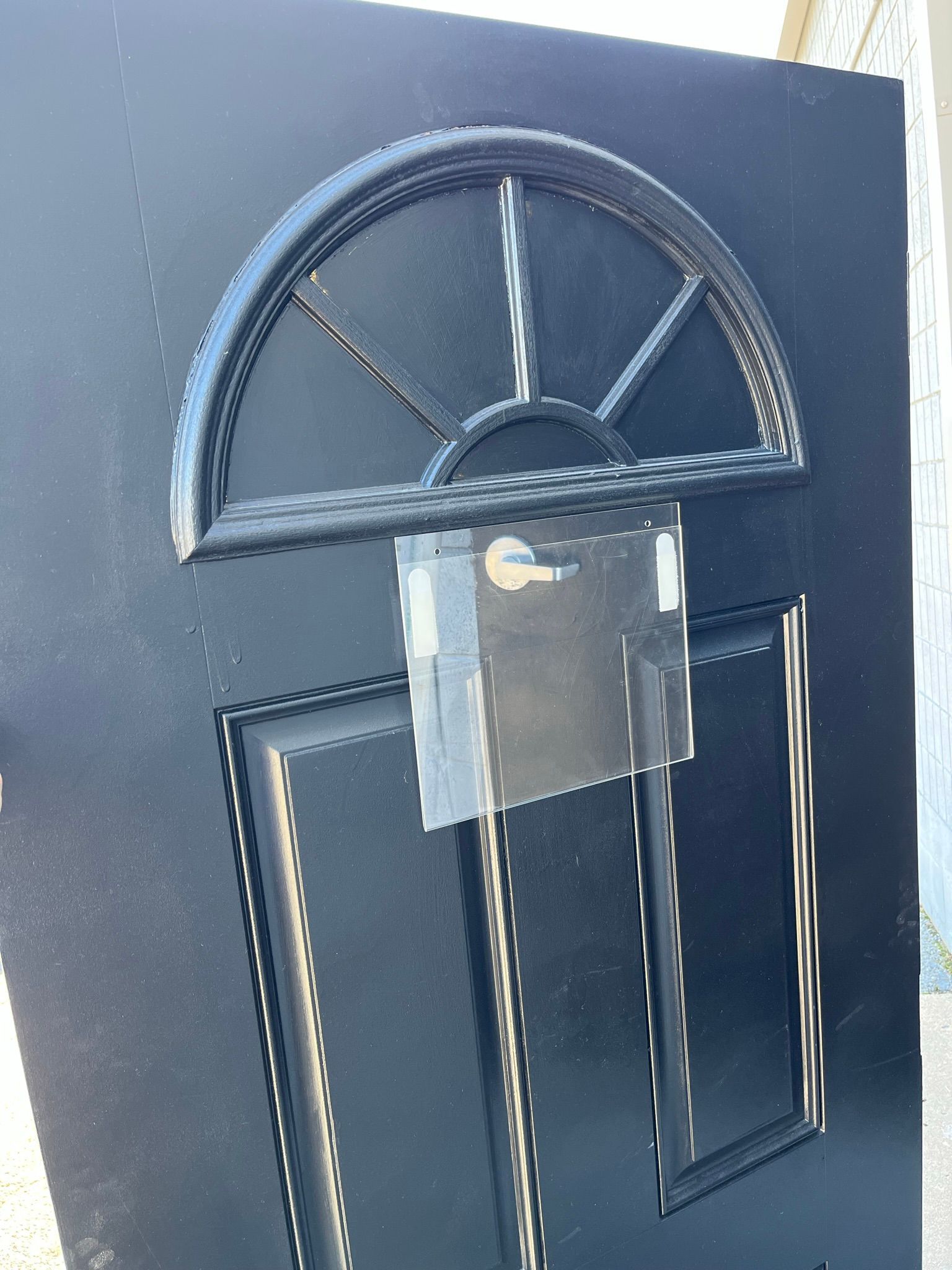 Black front door with arched window detail, door handle, and taped note.