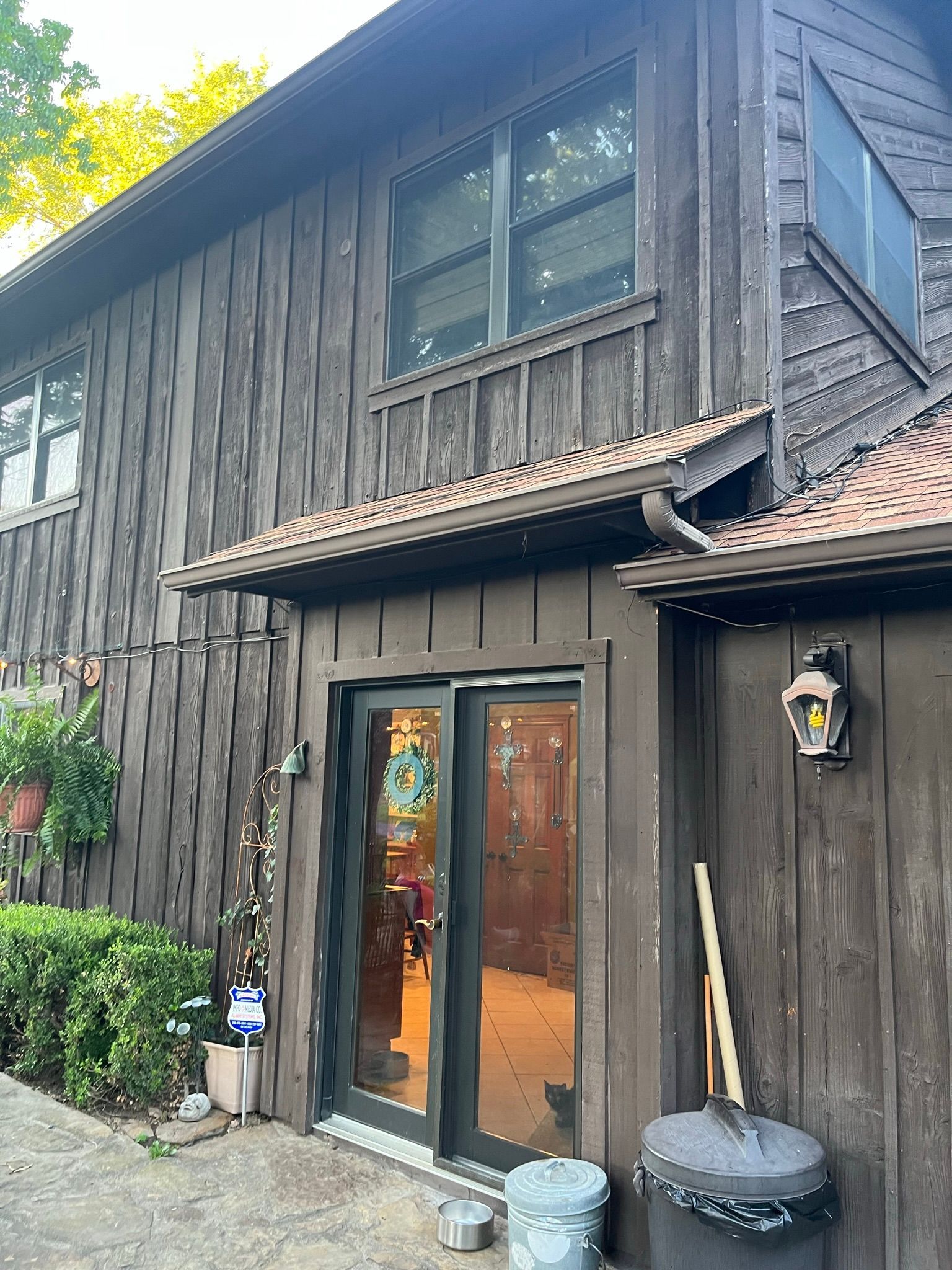 Brown wooden house with glass sliding doors, dark trim, and a small tiled awning.