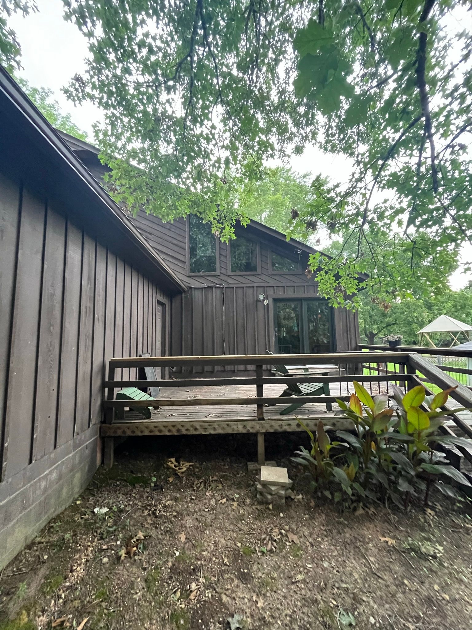 Brown-sided house with deck, surrounded by trees.