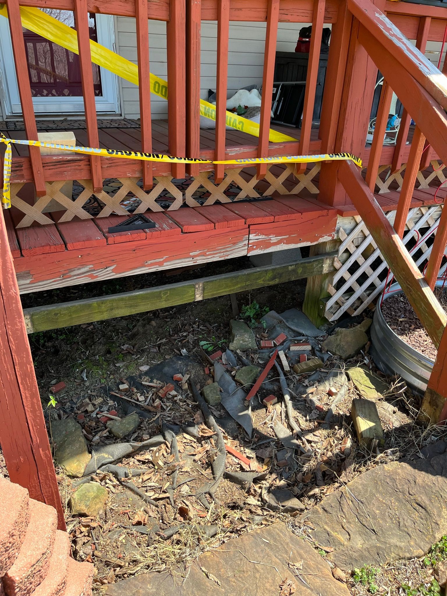 Damaged wooden porch with fallen debris, closed off with caution tape.