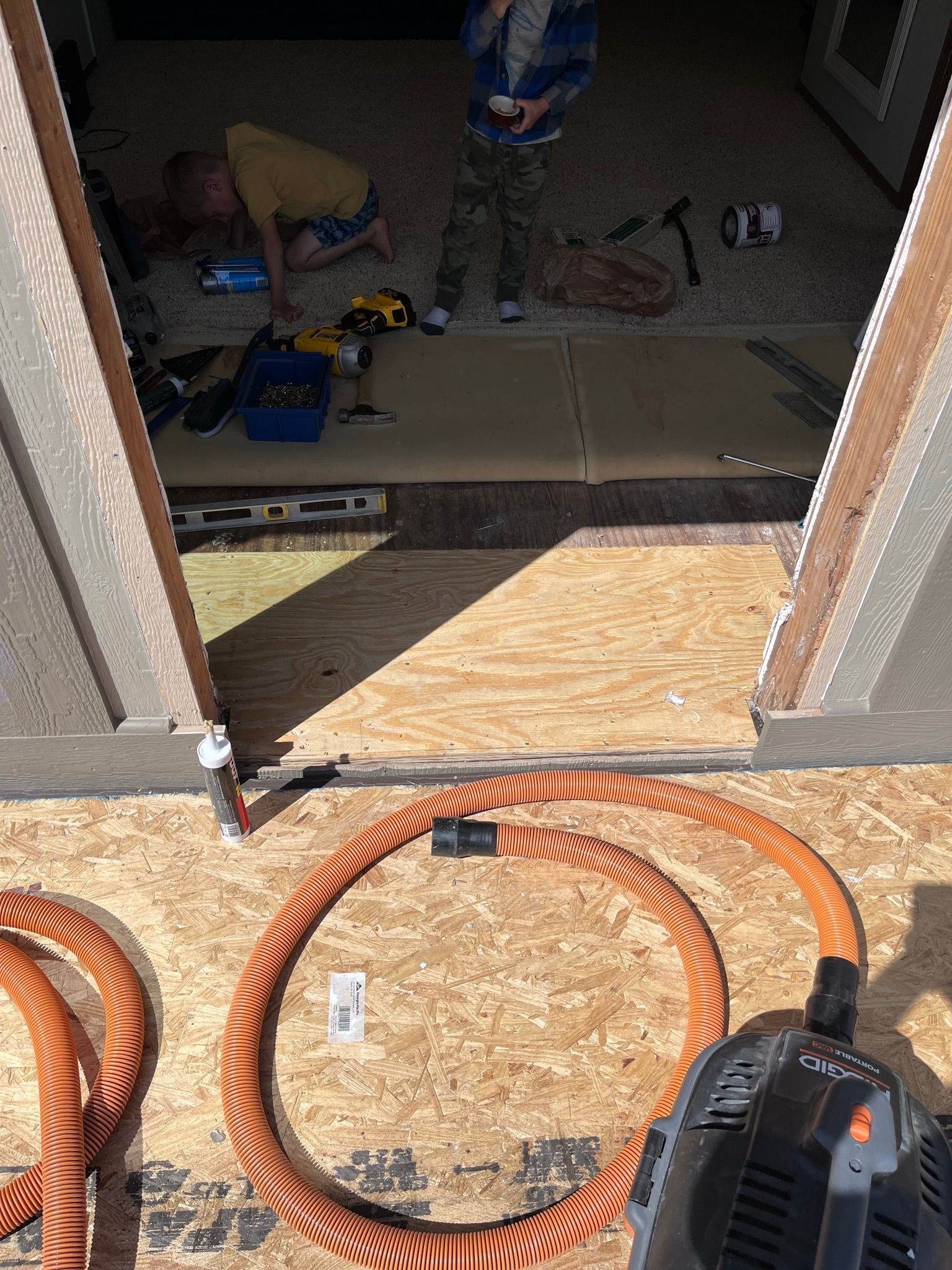 People inside shed laying flooring, with orange hose and tool in foreground.