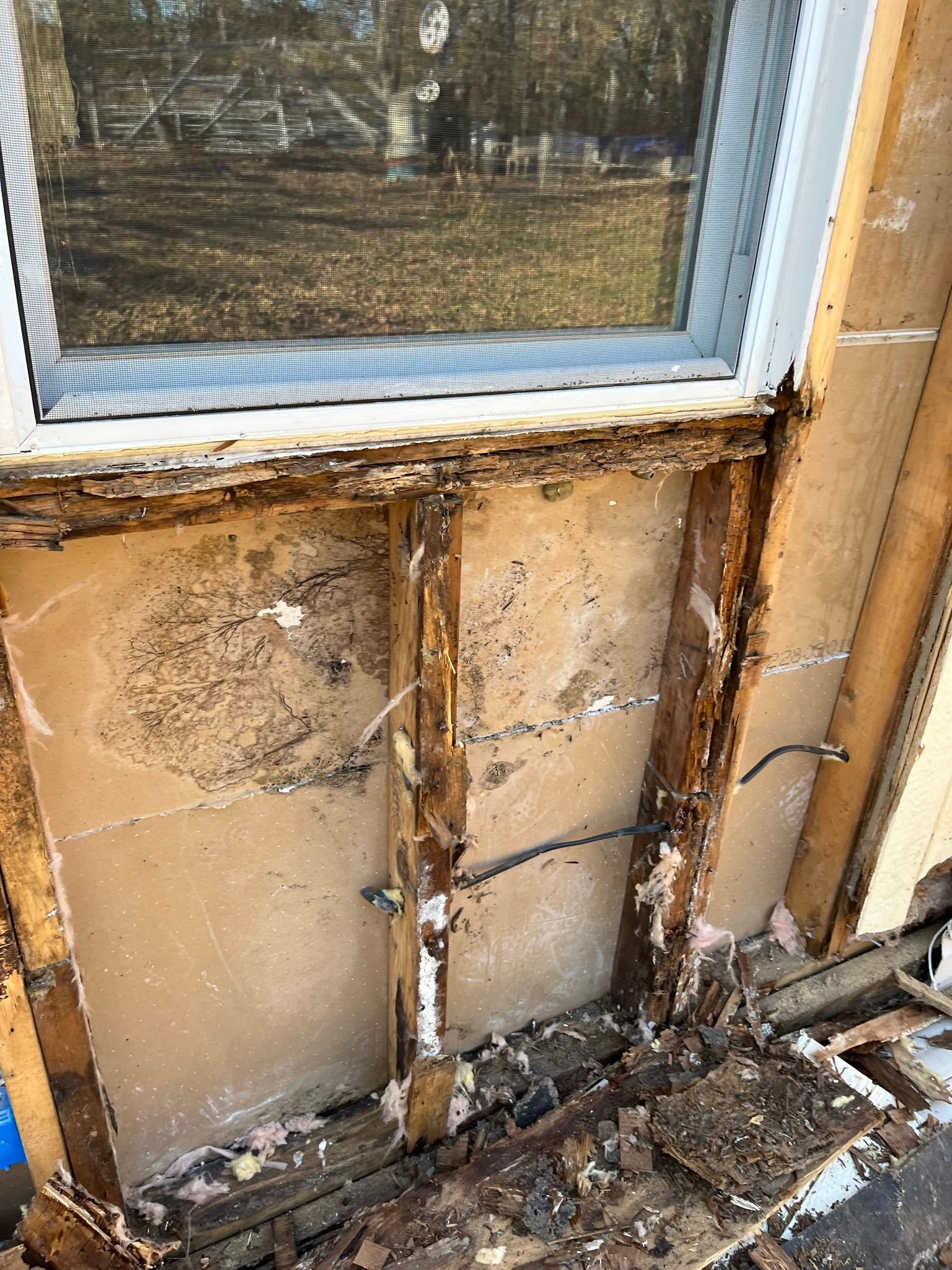 Damaged house wall with rotted wood around a window; exposed interior, wires visible.