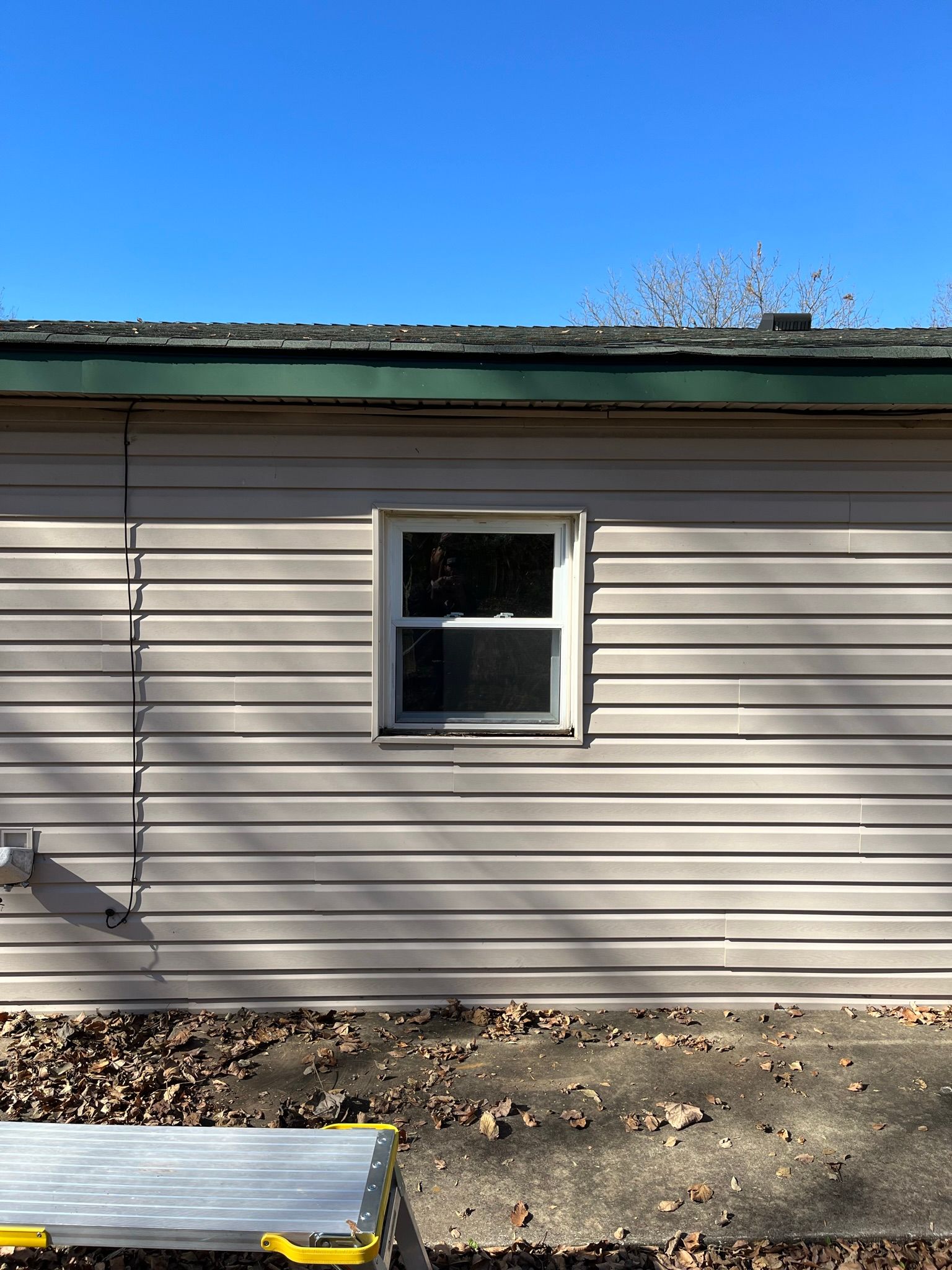 Tan siding with a small window, beneath a roof and a clear blue sky.