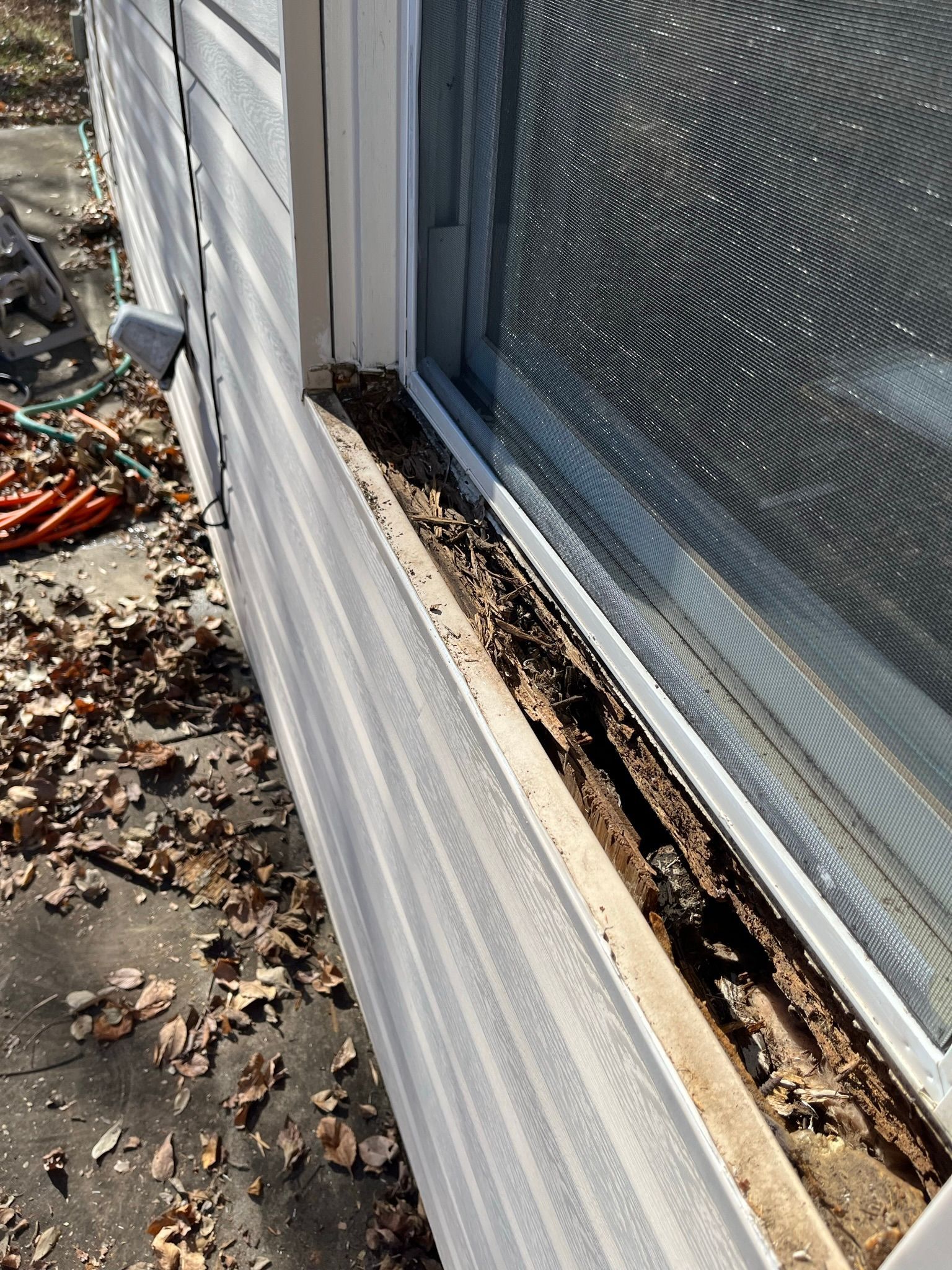 Damaged window frame on a house exterior, with exposed wood and debris. White siding and window frame.