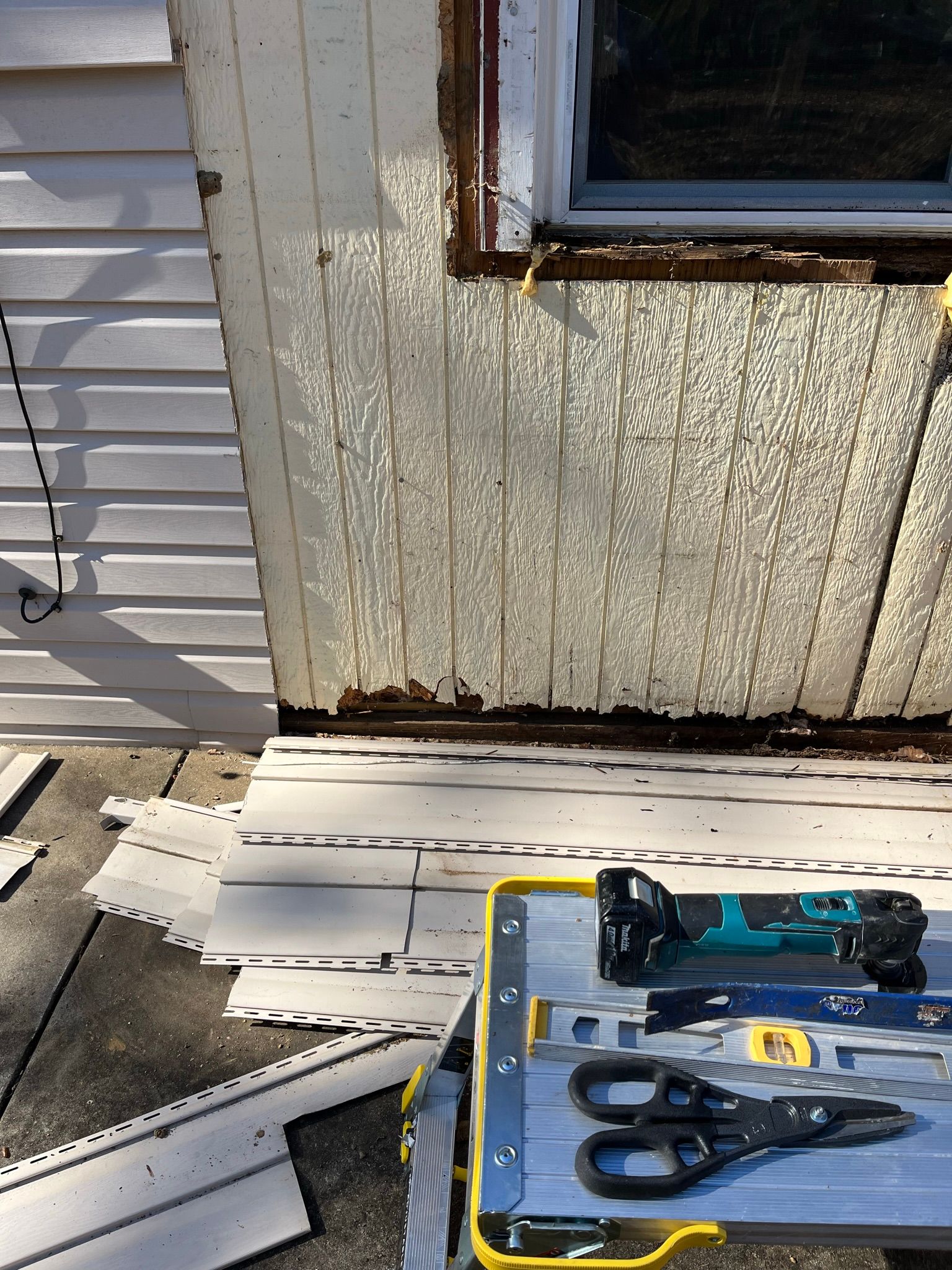 Exterior house siding repair in progress; peeling paint, tools on a work table.