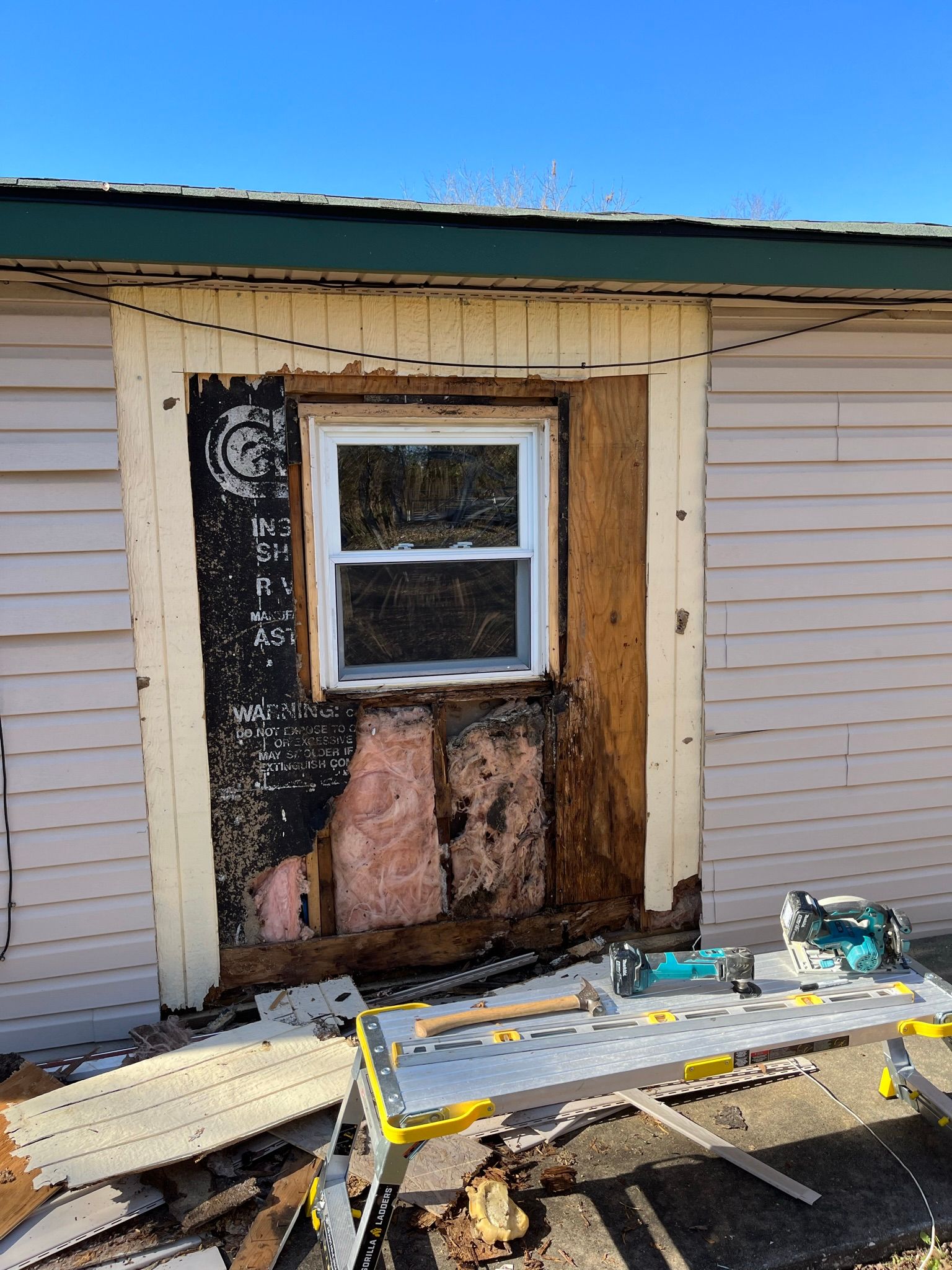 Exterior wall with a window undergoing renovation. Partially stripped siding and exposed framing.