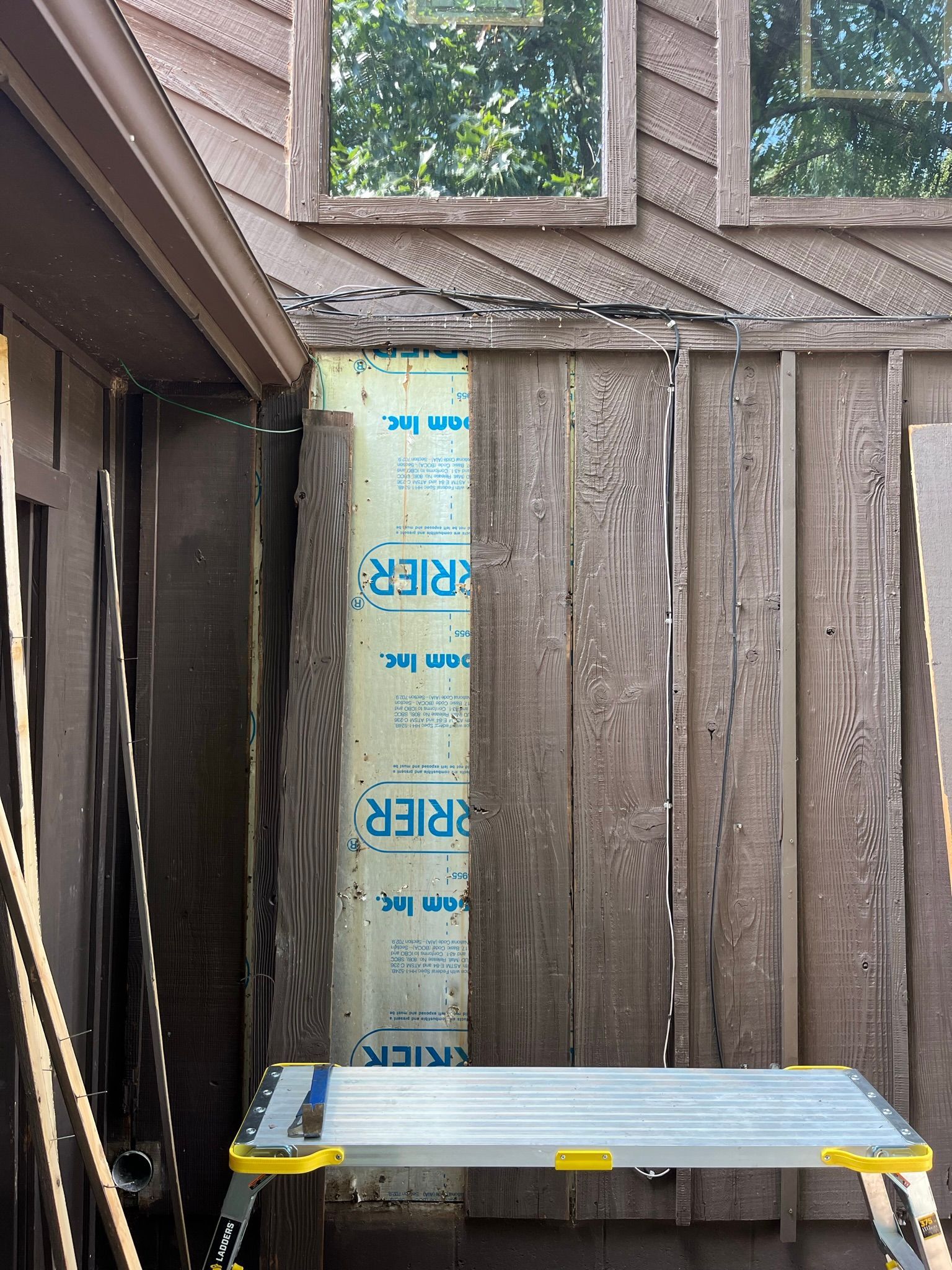 Exterior wall with exposed insulation and siding partially removed. A stepladder is positioned below.