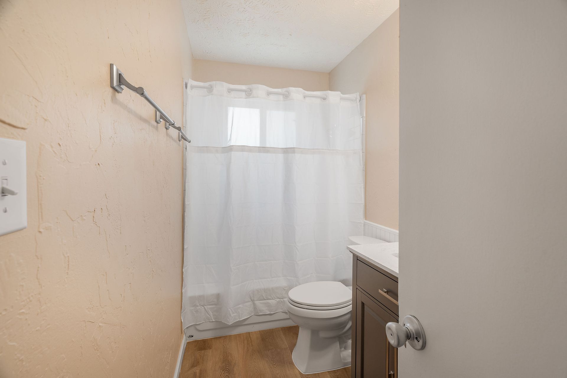 Bathroom with a toilet, shower with curtain, and vanity. Beige walls, wood-look floor.