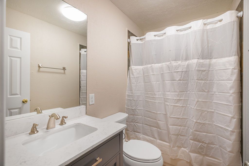 Bathroom with a white vanity, toilet, and shower with a white curtain.