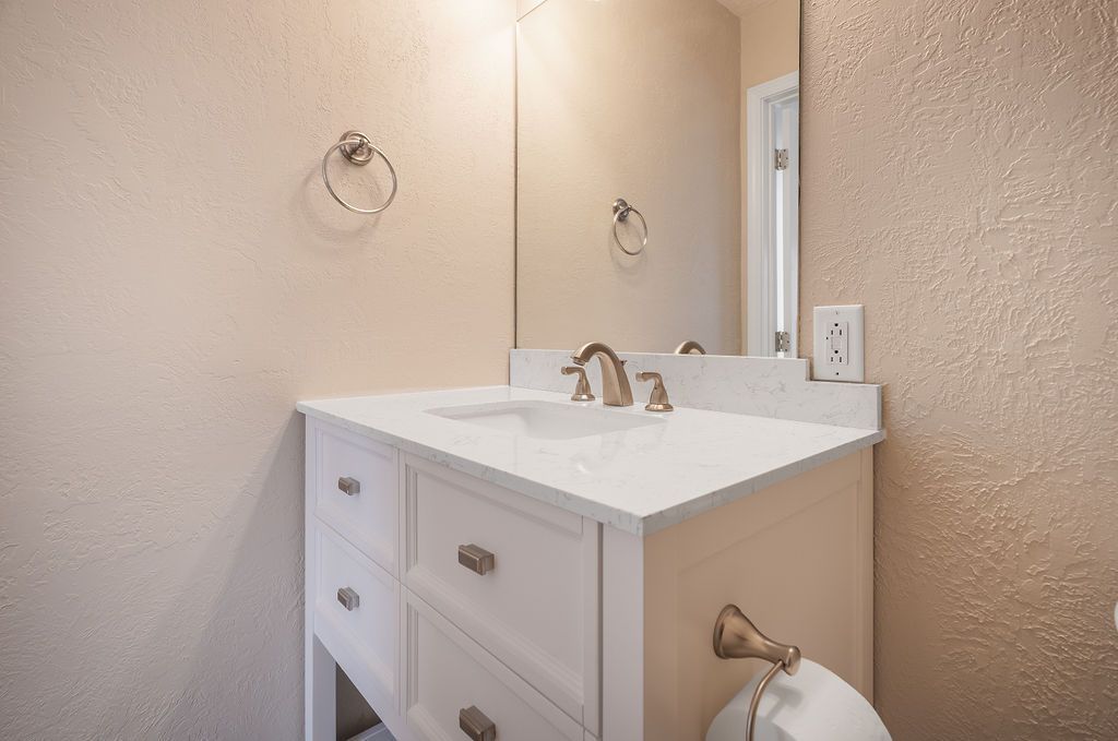 White bathroom vanity with a white countertop and gold fixtures.