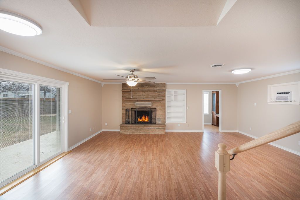 Spacious living room with fireplace, sliding glass door, and wooden floor. Empty and well-lit.