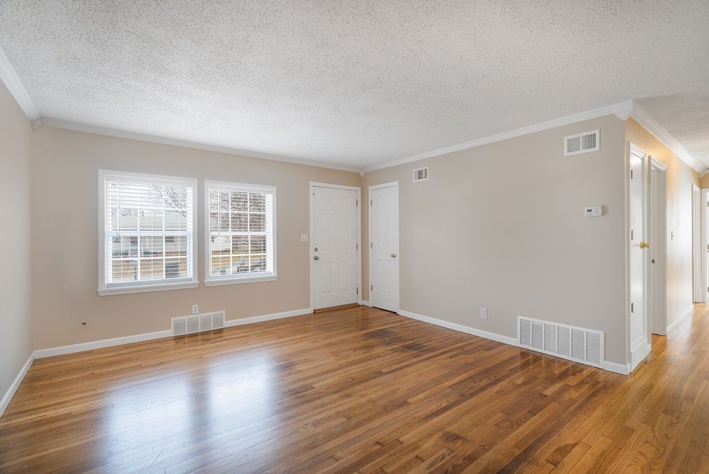 Empty room with hardwood floors, white trim, two windows, and neutral walls.