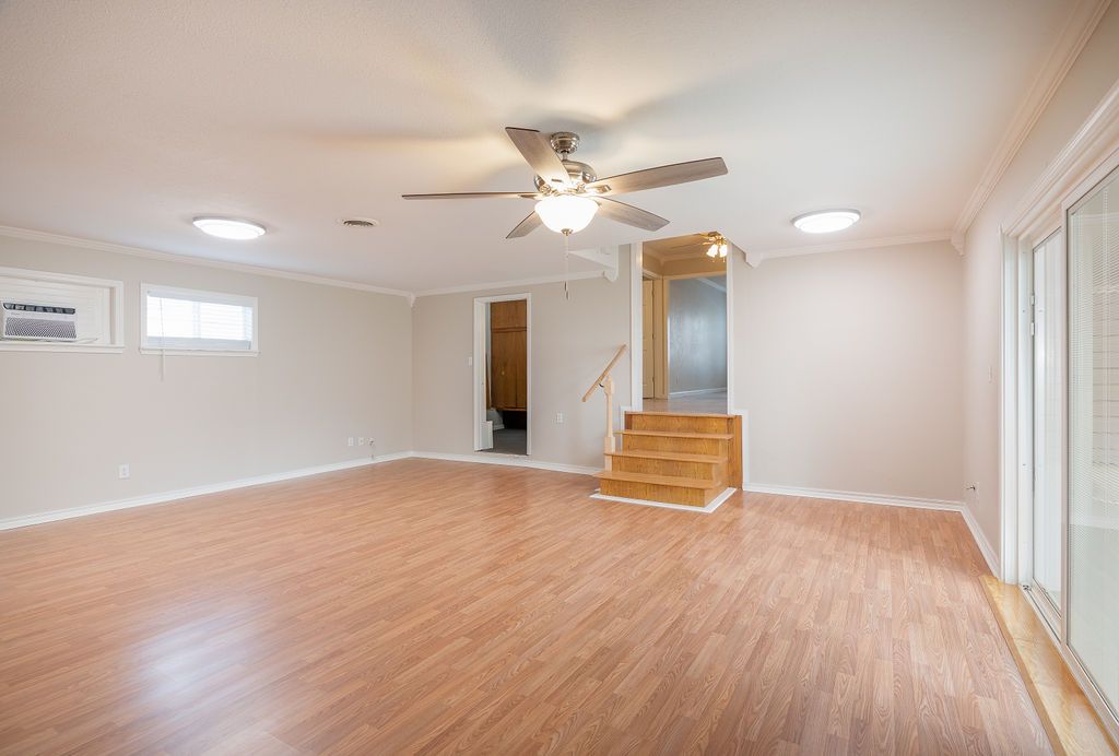 Empty room with wood-look flooring, recessed lights, ceiling fan, and sliding glass door. Stairs lead upward.