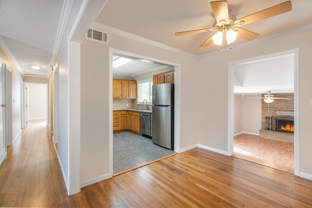 Interior view of a house with hardwood floors, doorways to kitchen and living room with fireplace, and a hallway.