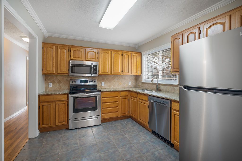 Kitchen with stainless steel appliances, light wood cabinets, and gray tile flooring.