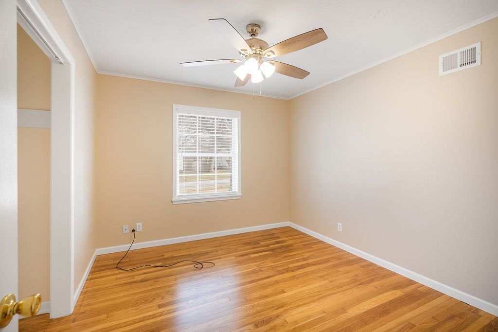 Empty room with hardwood floors, window, ceiling fan, and beige walls.