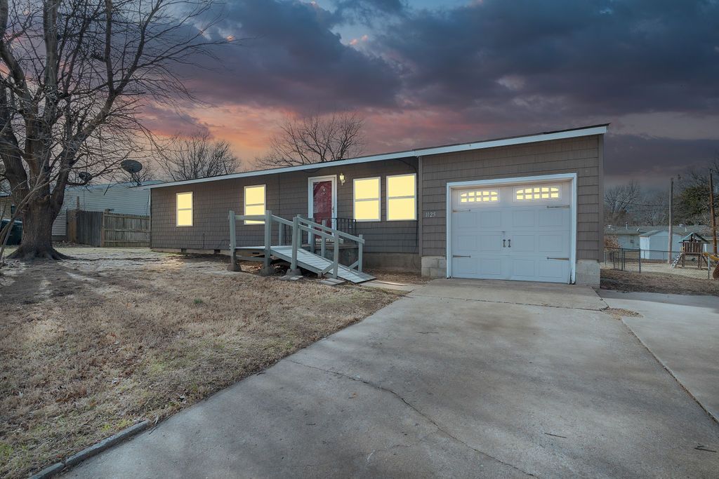 Ranch-style house with garage, driveway, and front steps, set against a colorful dusk sky.