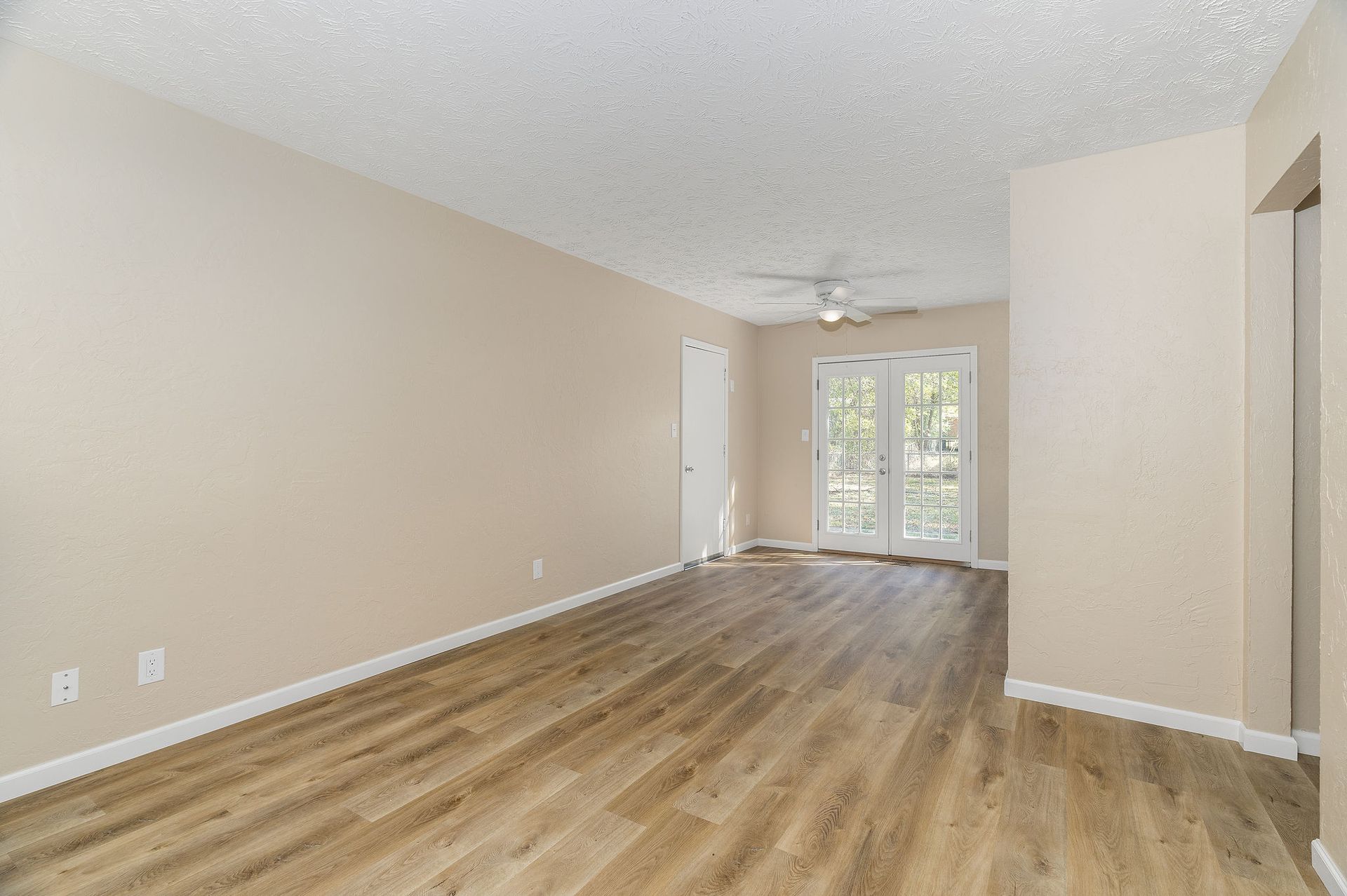 Empty living room with wood-look flooring, beige walls, and French doors leading outside.