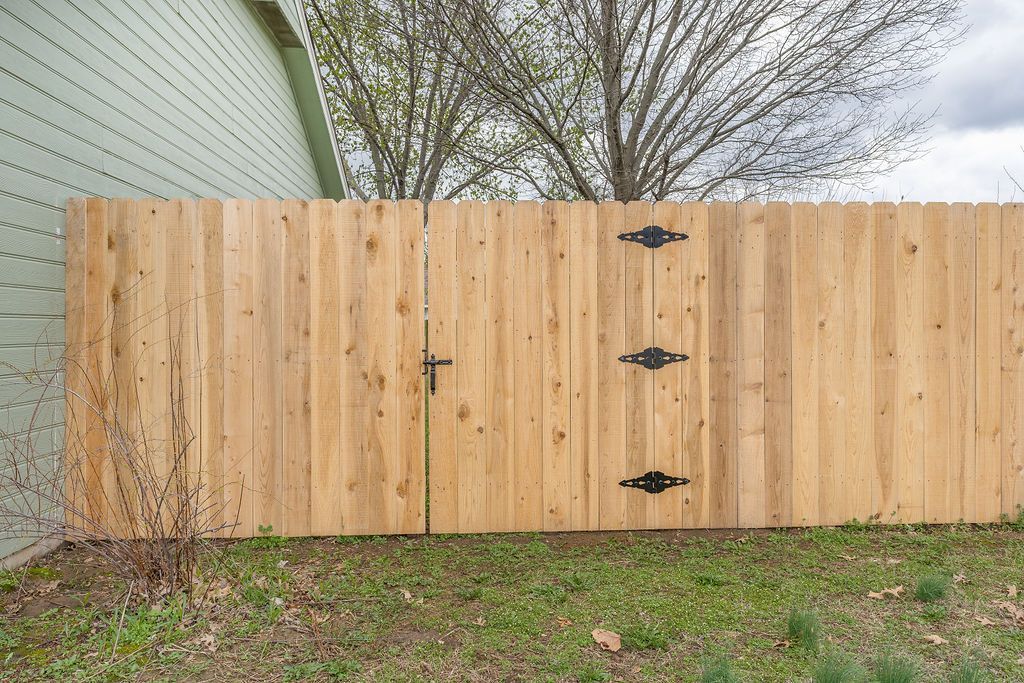 Wooden fence with gate, black hinges and handle, green siding on left.