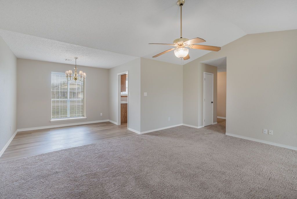Empty room with beige carpet, ceiling fan, and chandelier; light-colored walls and door.