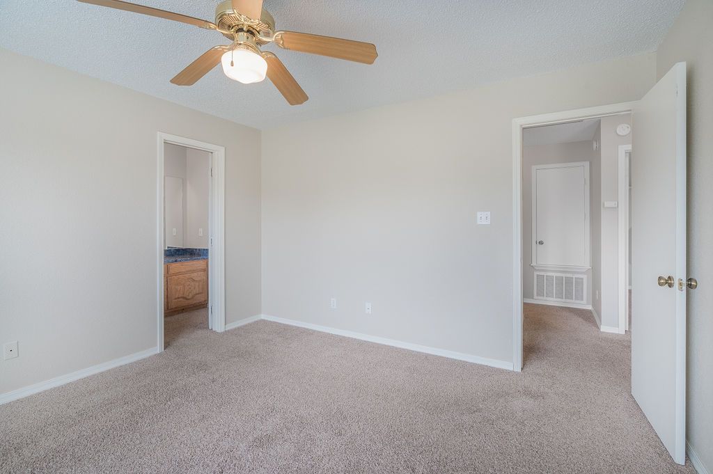 Empty bedroom with neutral walls, carpet, ceiling fan, and open doorways to other rooms.