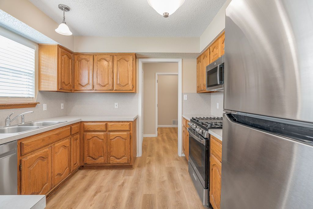 Kitchen with wooden cabinets, stainless steel appliances, and wood-look flooring.