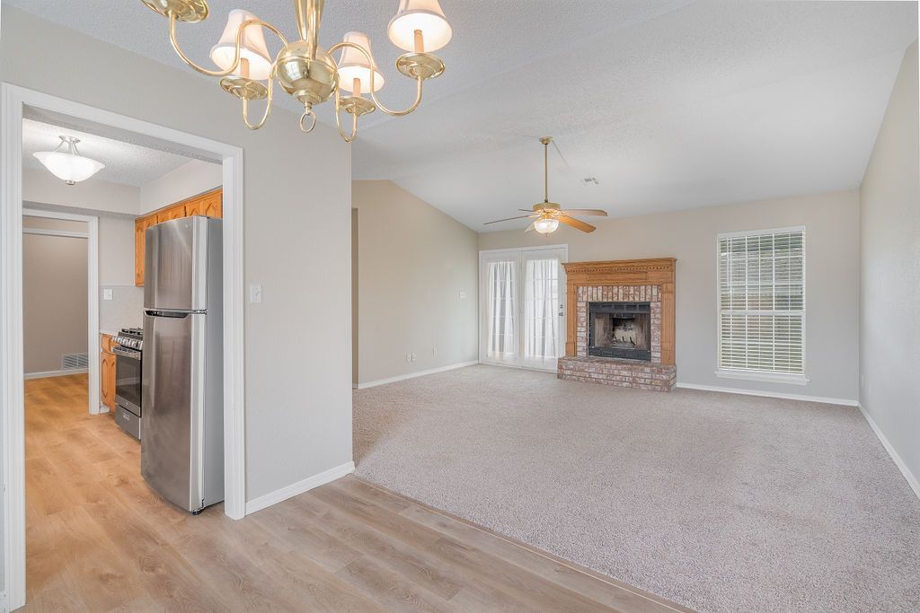 Interior view of a living room with a fireplace, chandelier, and a view into the kitchen.