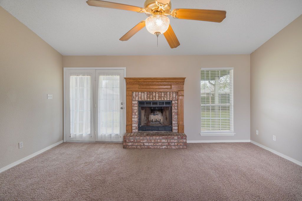 Empty living room with fireplace, sliding glass door, window, tan walls, and carpet.