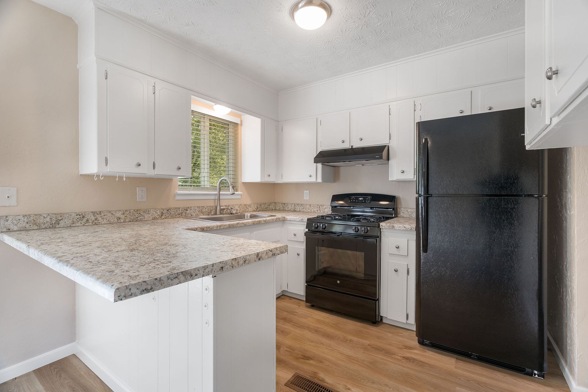 White kitchen with black appliances, light countertops, and wood-look flooring.