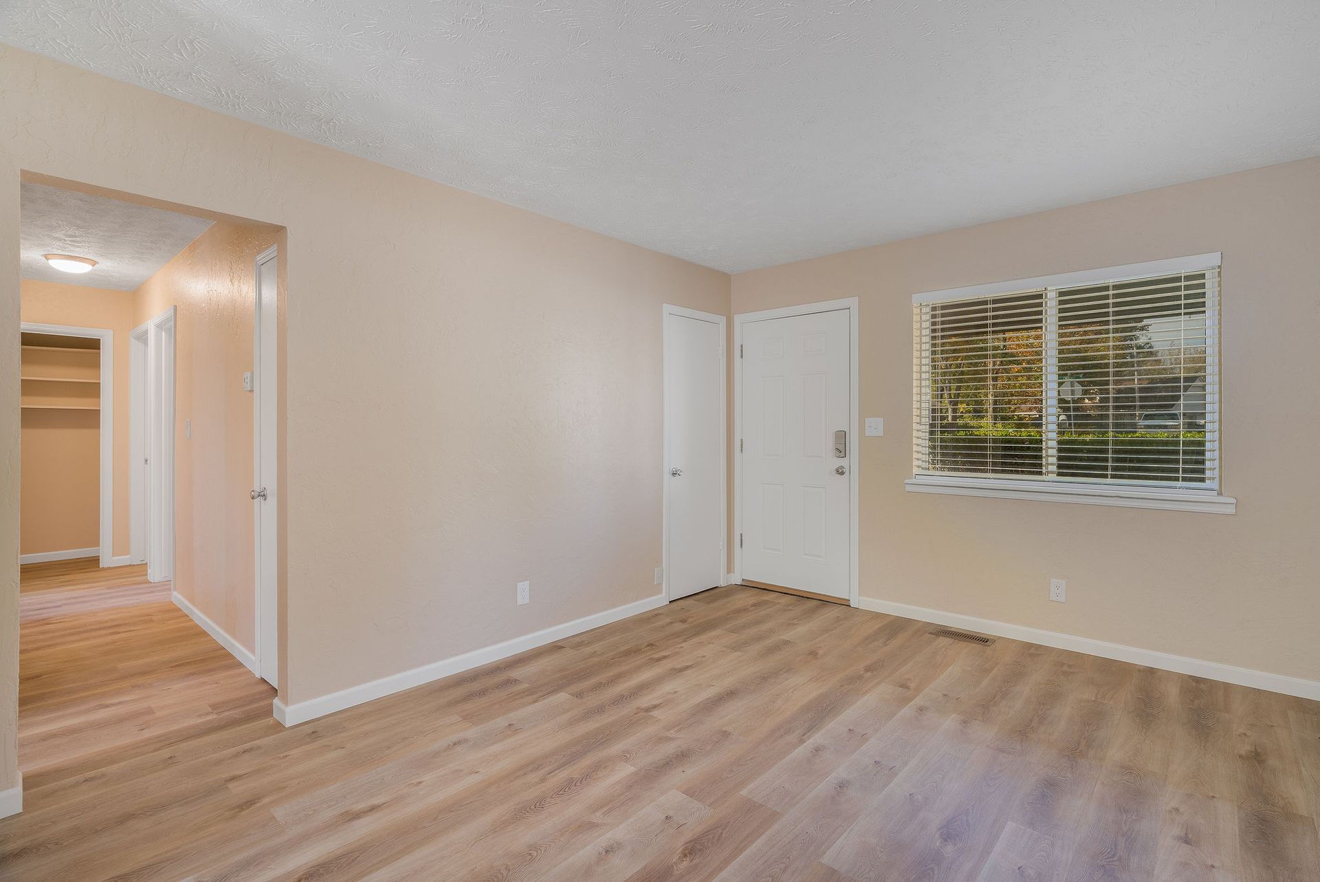 Interior view of a room with wood-look flooring, tan walls, a white door, and a window with a view.