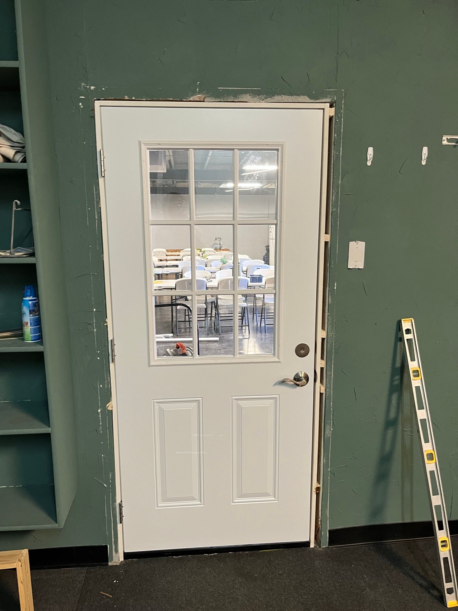 White door with glass panes, set in a green wall. Level leaning against the wall.