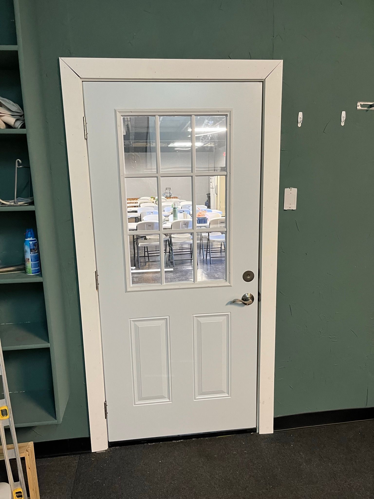 White door with glass panes in a green-painted room. A shelf is to the left.