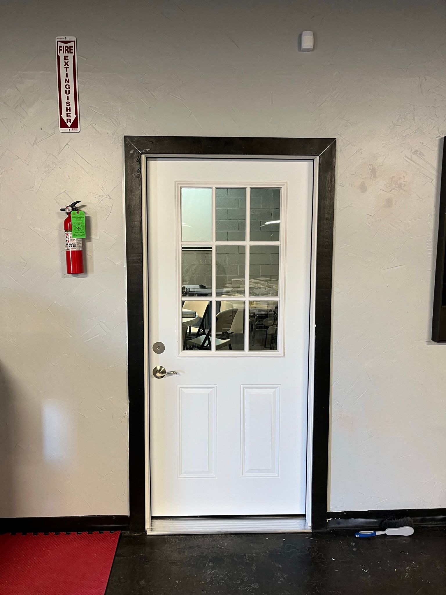 White door with glass pane, black frame, and fire extinguisher on a wall.