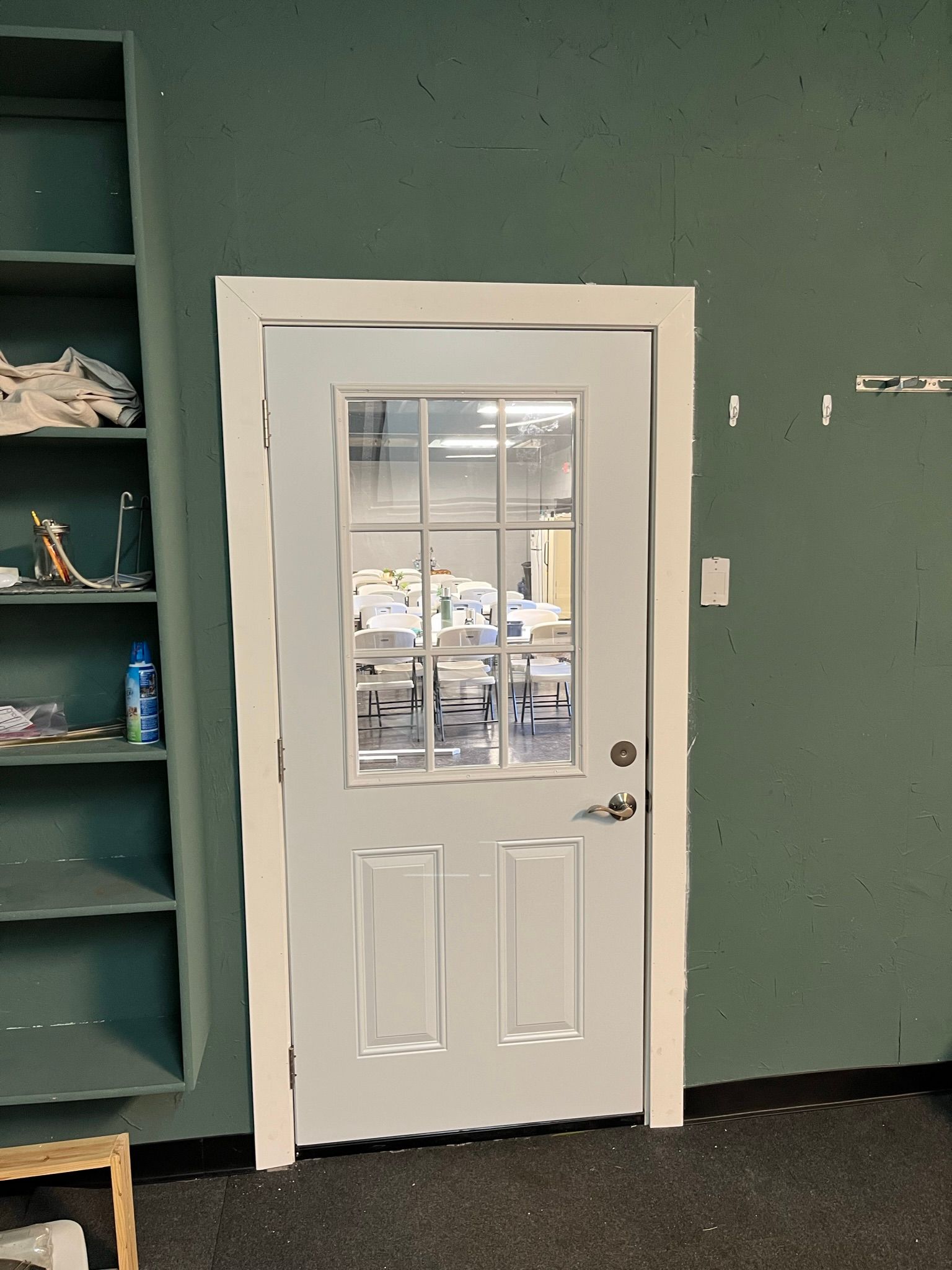 White door with glass panes in a green-painted room, with a shelf on the left.