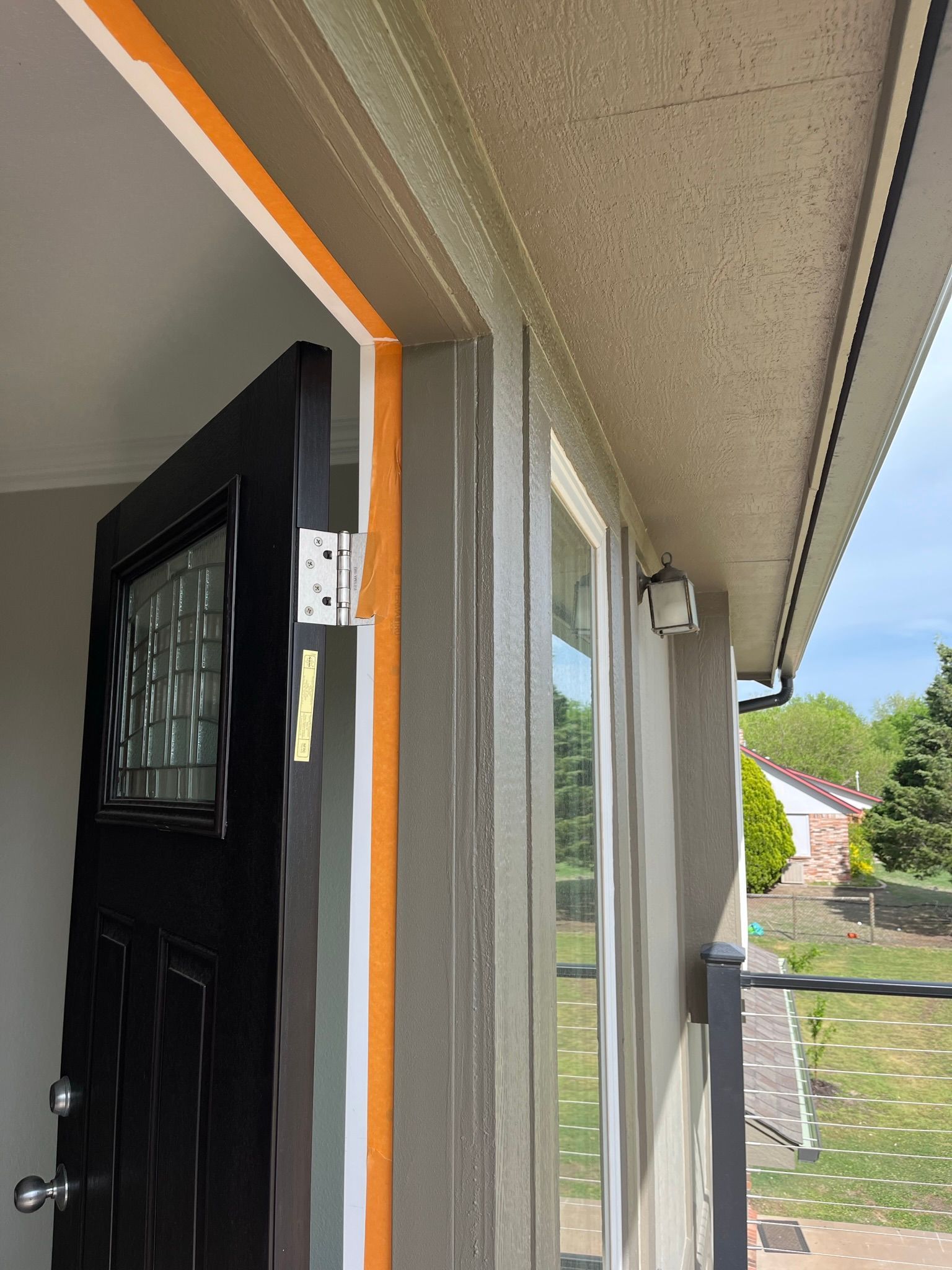 Black door with white hinges, orange and white tape on frame. Beige exterior with window and security camera.