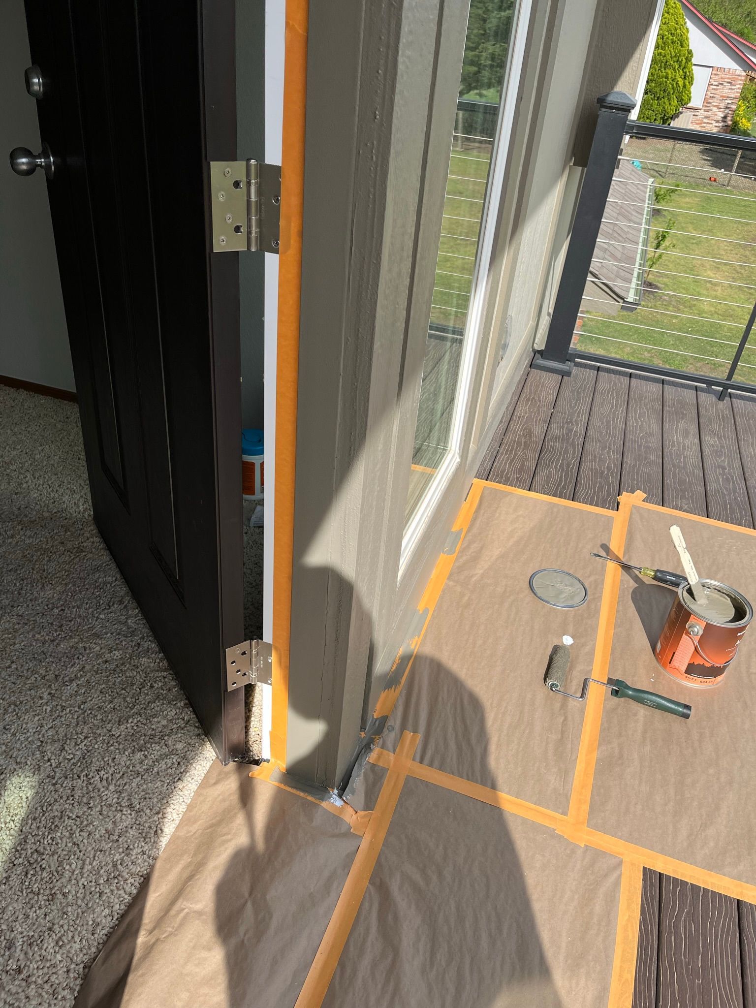 Door frame being painted; masking tape on the deck and door, paint can and tools nearby.