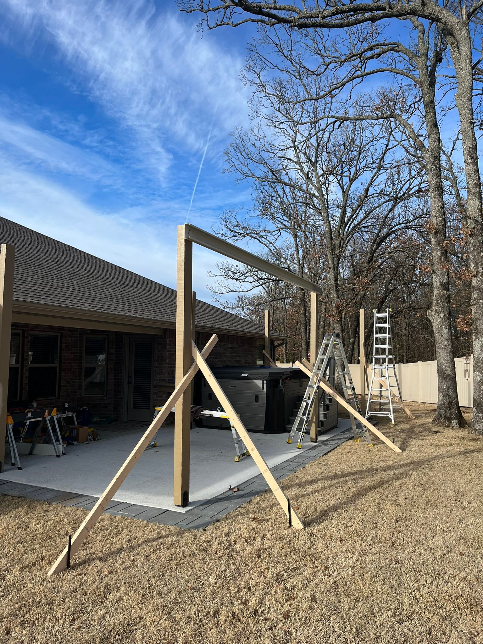 Wooden structure under construction on a concrete patio next to a house. Supports are in place.