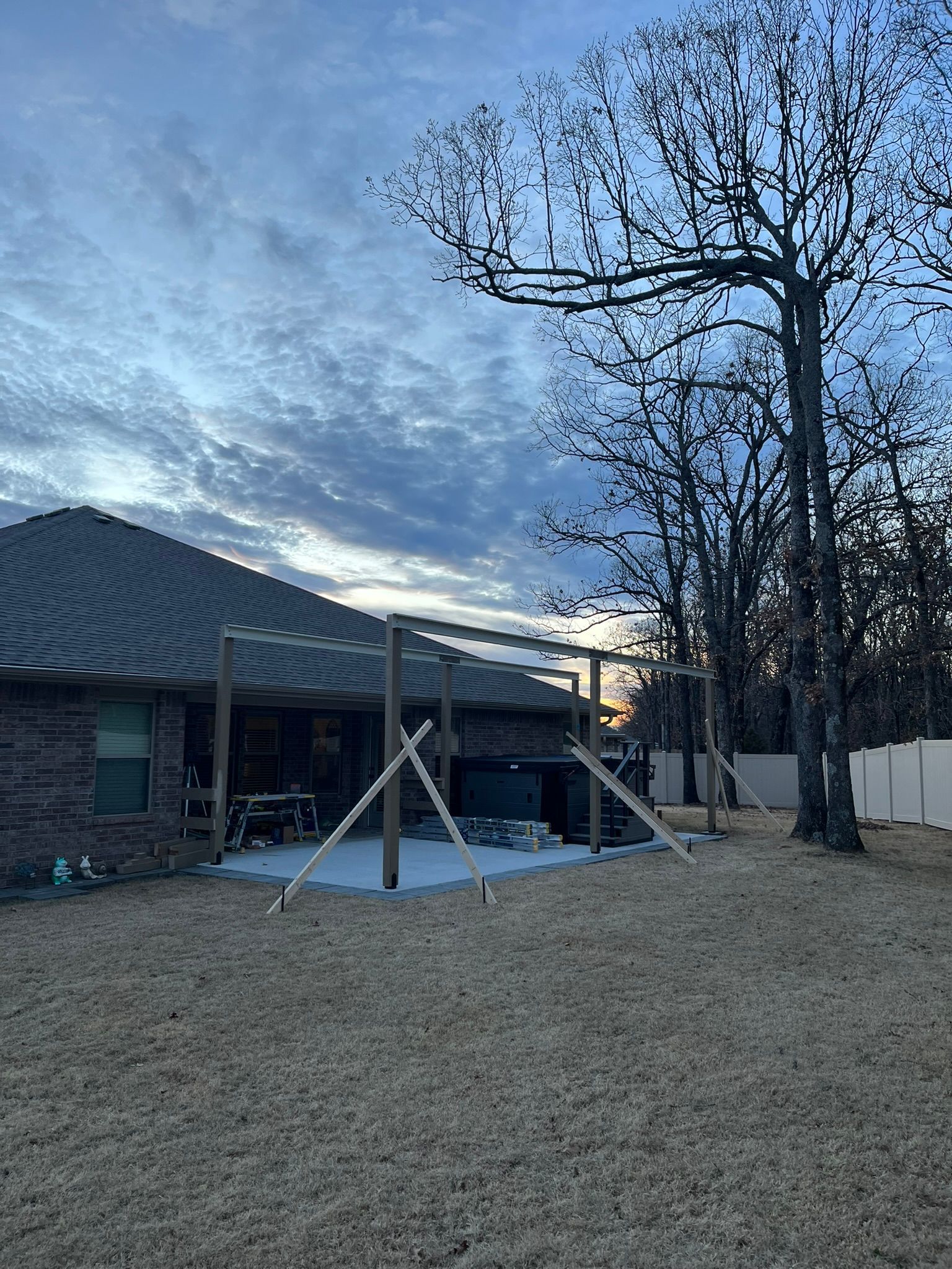 Backyard with a partially built pergola extending from a brick house, under a cloudy sky.