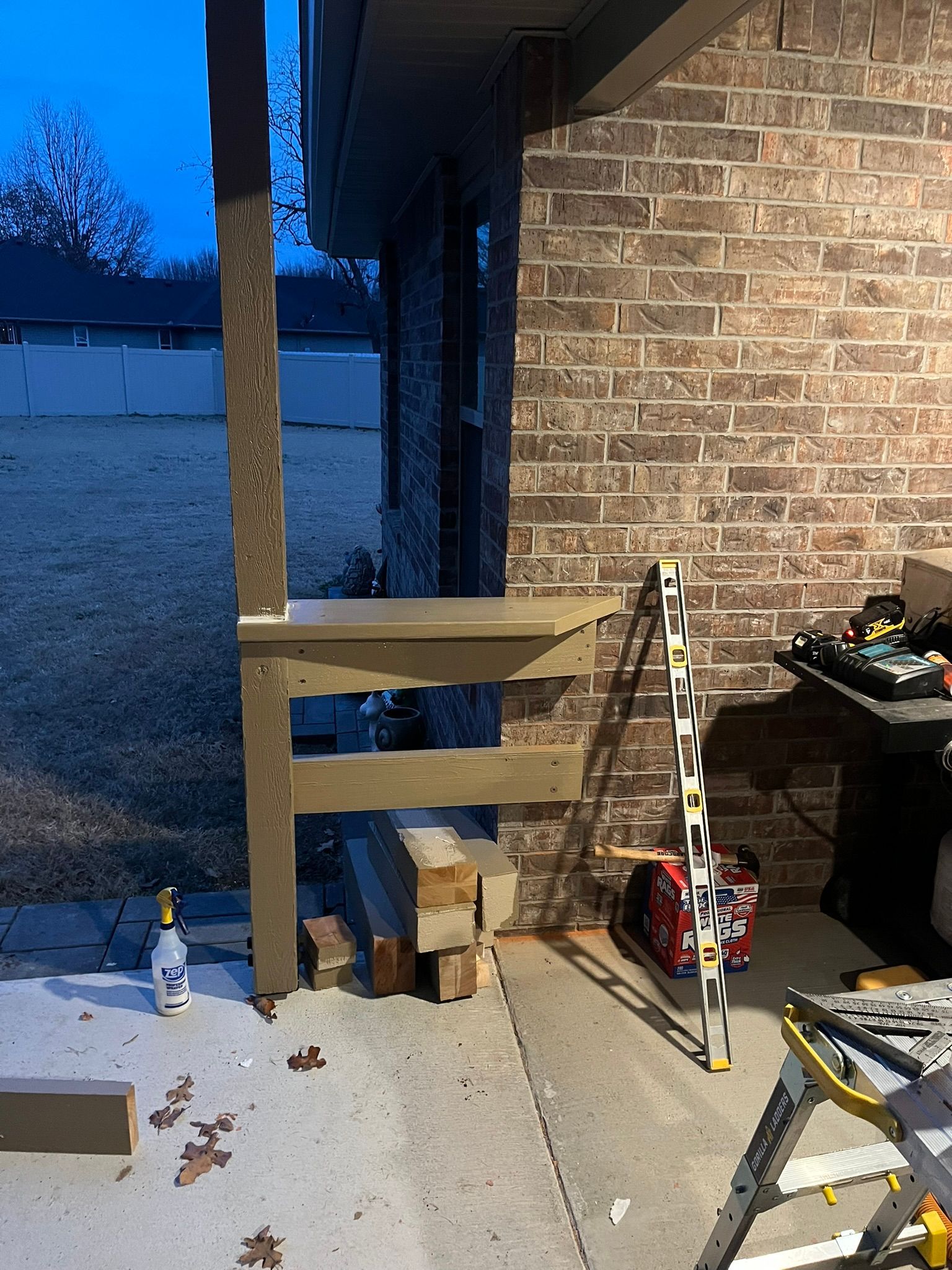 Wooden structure being built against a brick wall and a support post. Construction tools and materials visible.