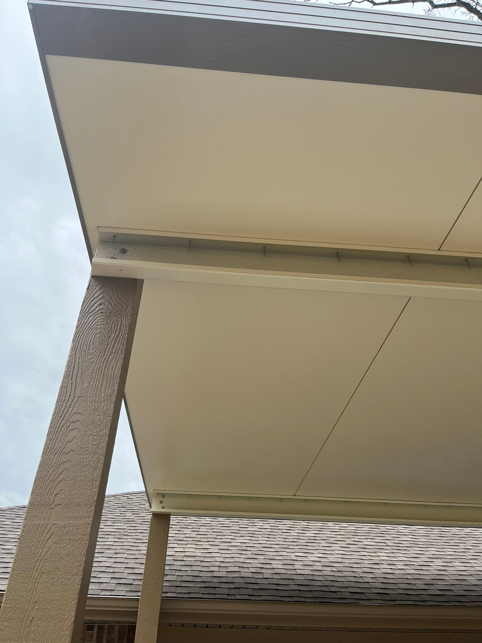 Beige covered patio roof with a support column, cloudy sky in background.