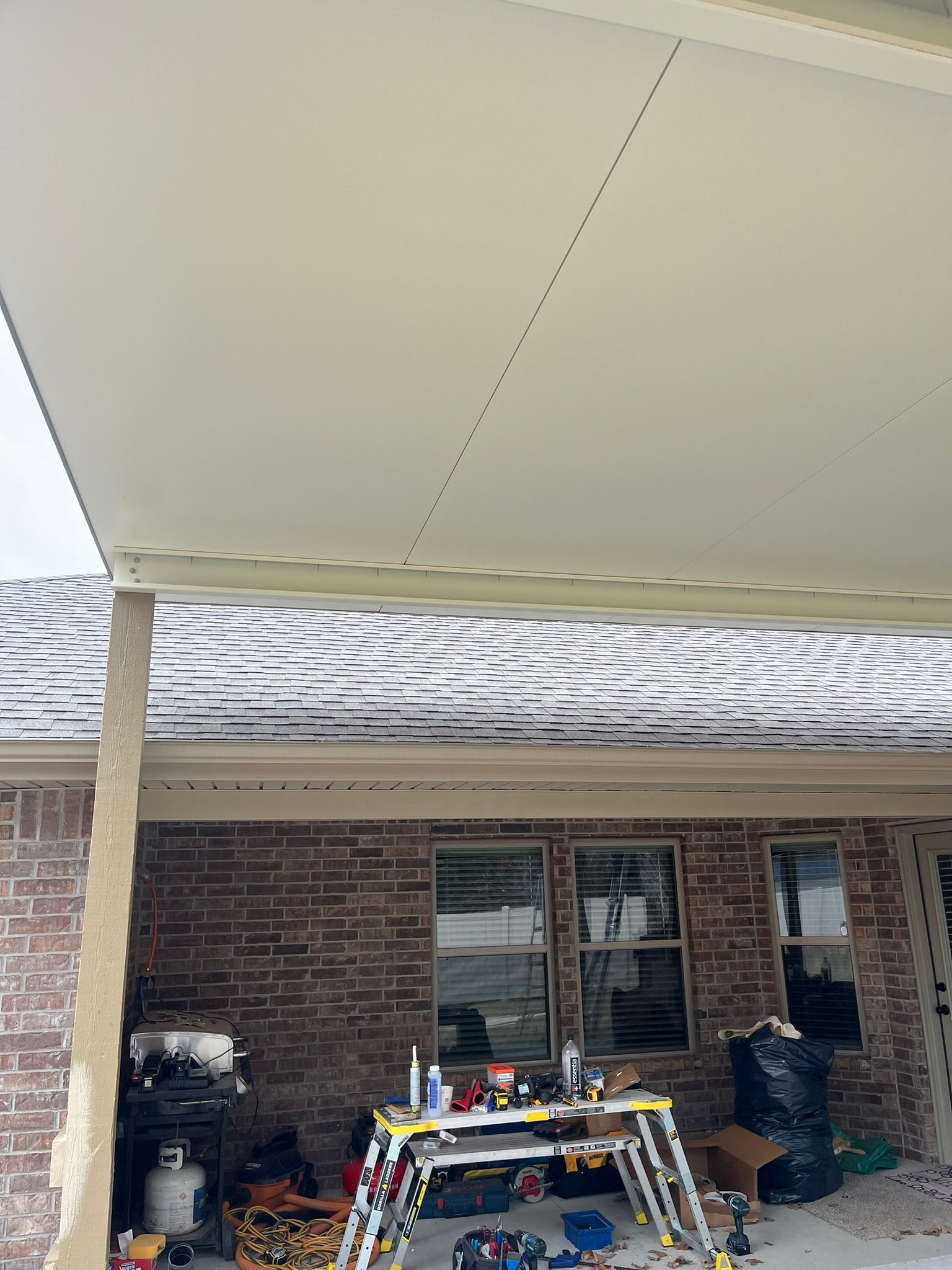 Patio cover over brick home, with snow on roof and work tools visible.