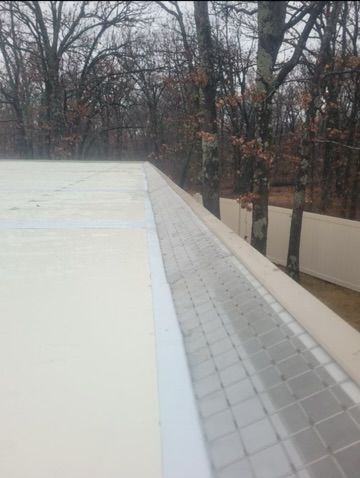 White rooftop edge with gutter, fence, and bare trees in the background.