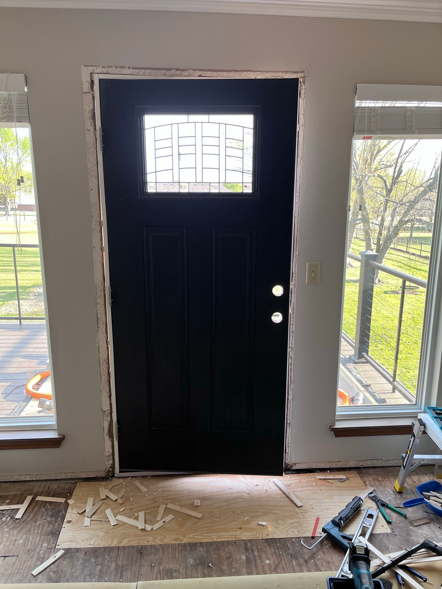 Black front door with glass window, set in white wall, flanked by two windows.