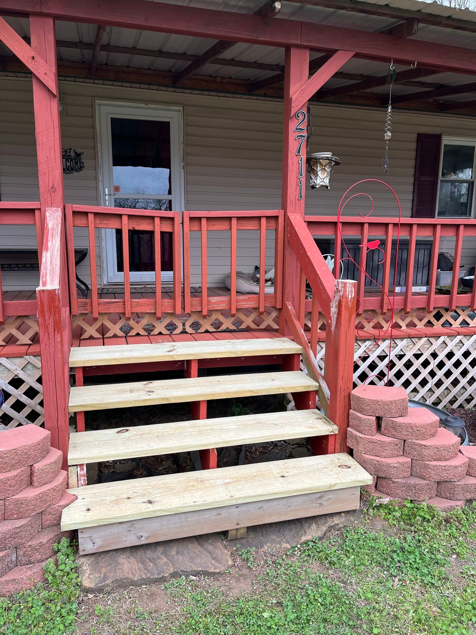 Red-painted porch with stairs leading to a white door. Brick border on the stairs' sides.