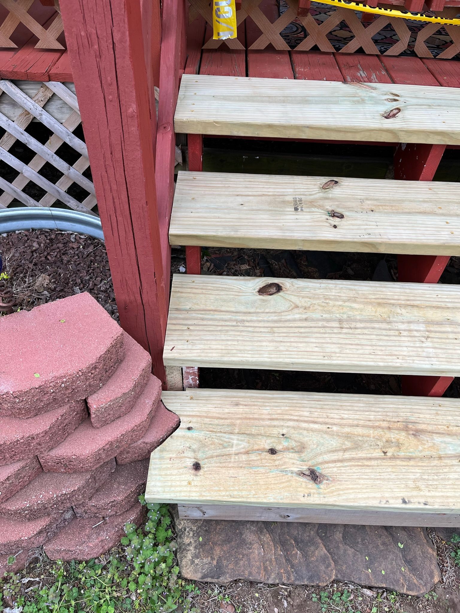 Wooden outdoor steps with damaged treads, painted red support structure, and brick retaining wall.
