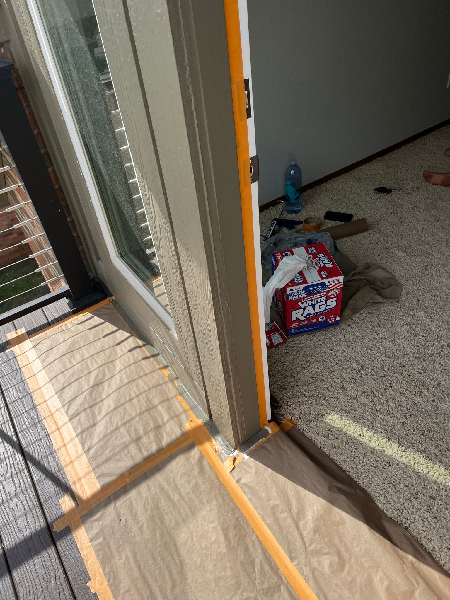A window frame with painter's tape and paper covering the flooring. A pile of items sits near the wall.