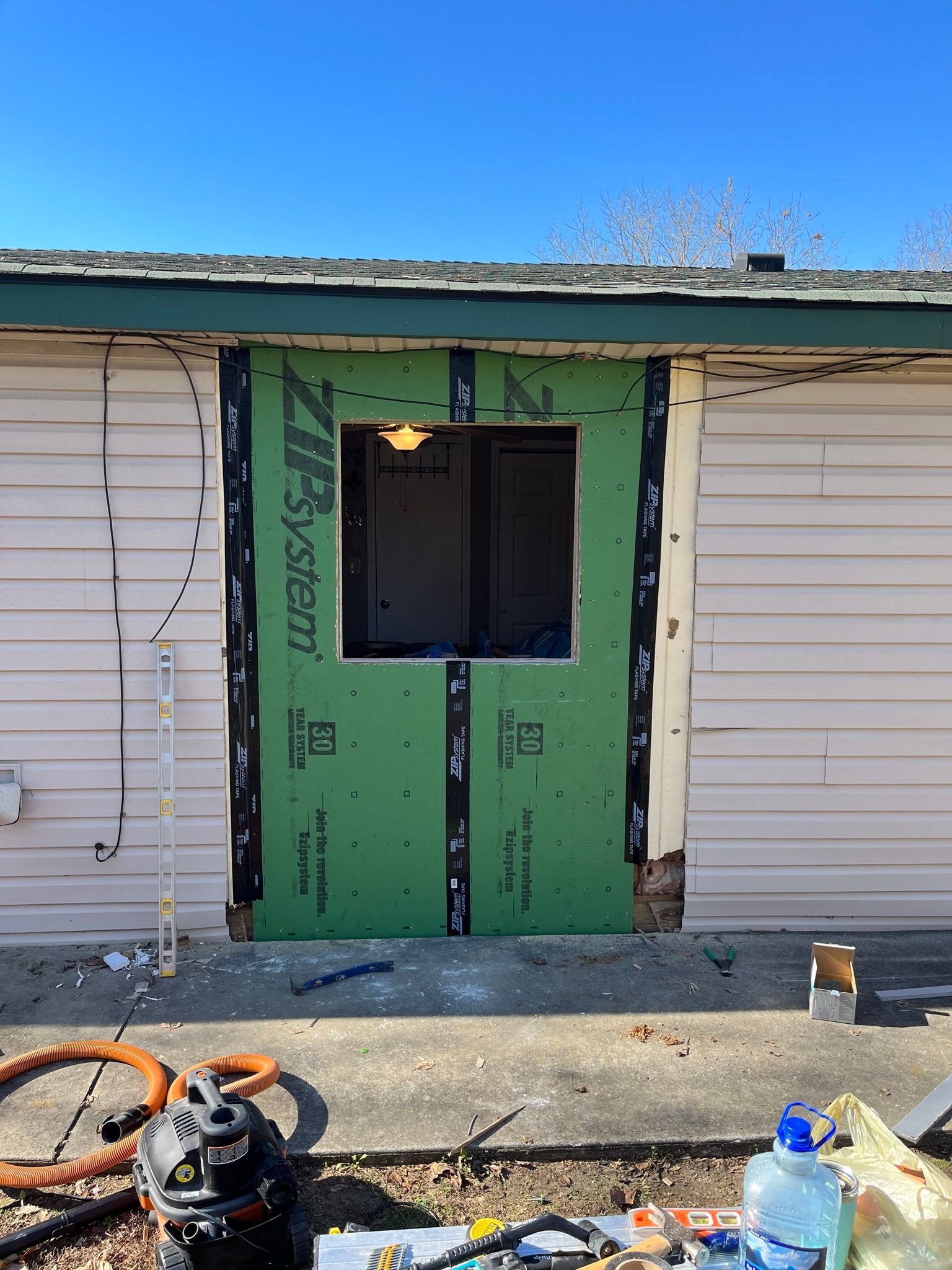 Exterior wall with a green rectangular opening framed by green sheathing, with a window or door space.