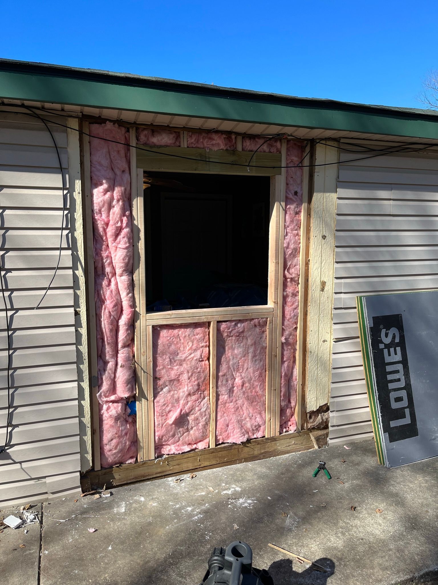 Exterior of a building with a window framed by wood and pink insulation. Siding visible.
