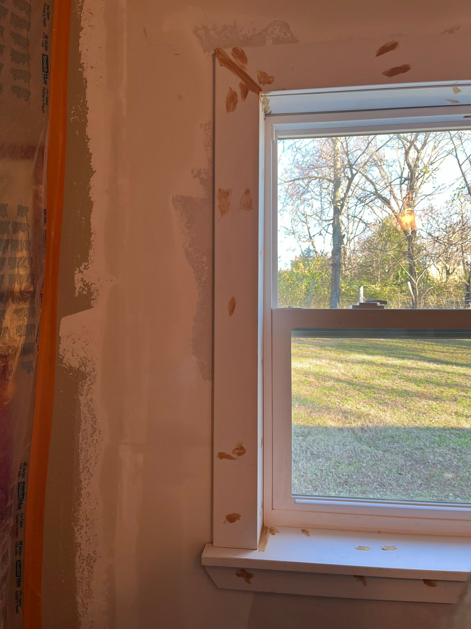 Corner of a room with a window. Drywall and window trim are being installed.