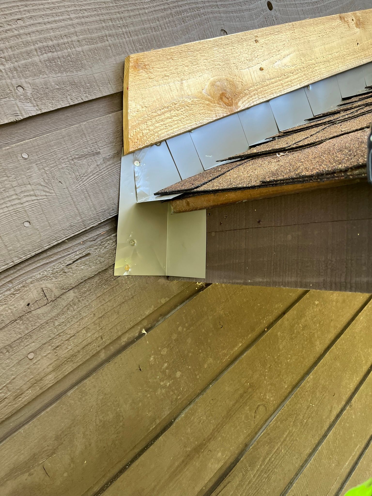 Close-up of a house corner with siding, roof shingles, and metal flashing.